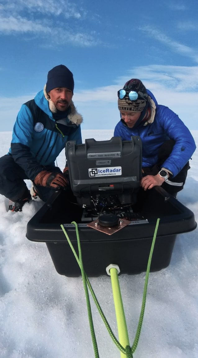 Matthieu et Heïdi sont agenouillés près du radar. Heïdi, à gauche du radar, regarde l'appareil alors que Matthieu, à droite, regarde la camera.